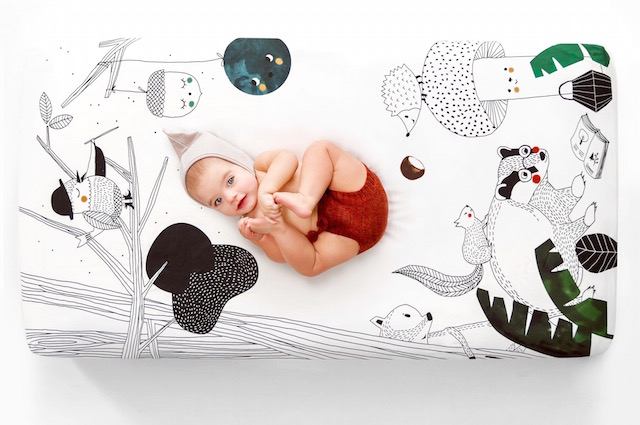 A baby laying on a play mat with black and white outdoor print.